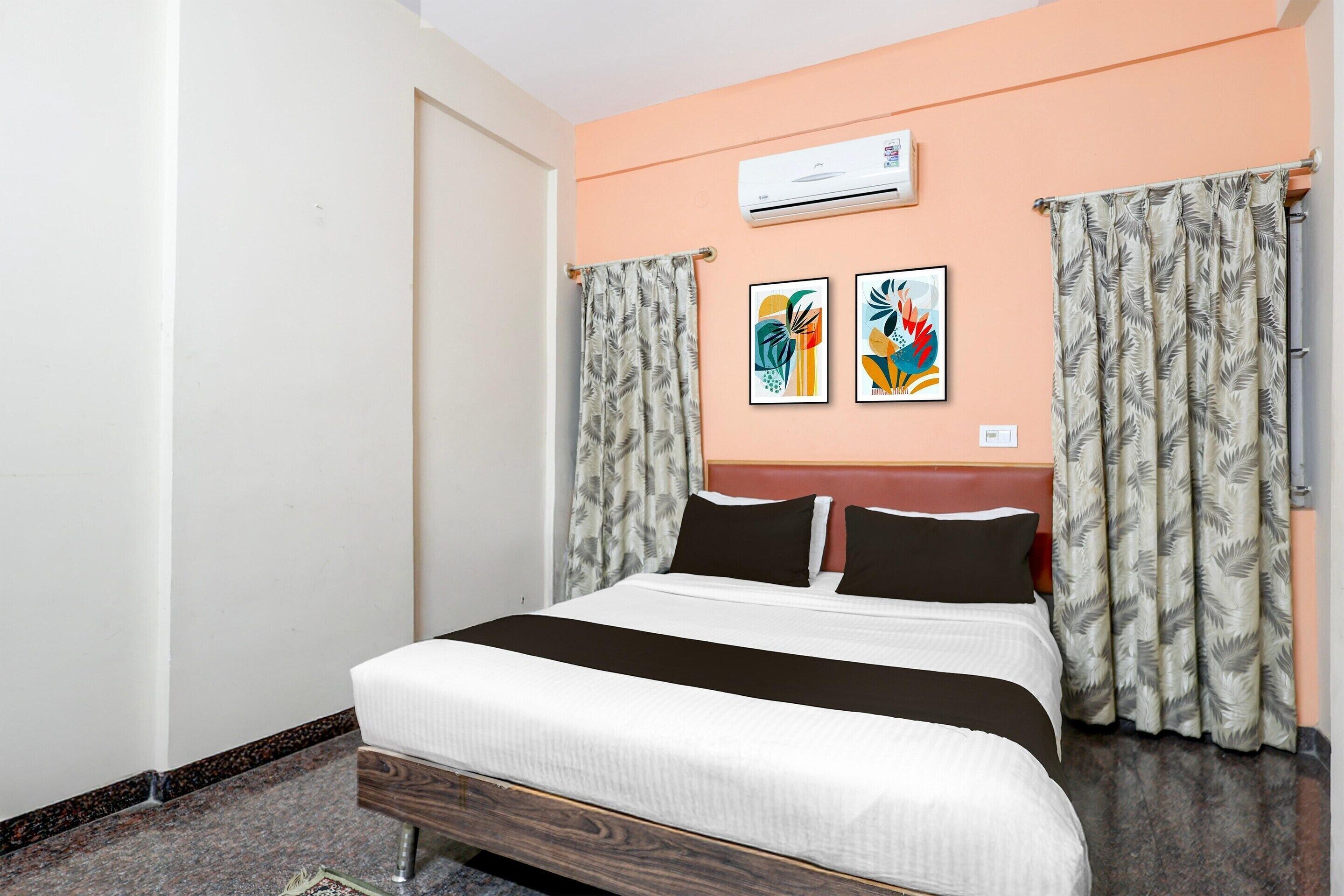 A hotel room with a bed, air conditioning unit, artwork, curtains, and a headboard.