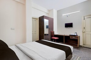 A hotel room with a bed, a desk, a chair, a television, and a door.