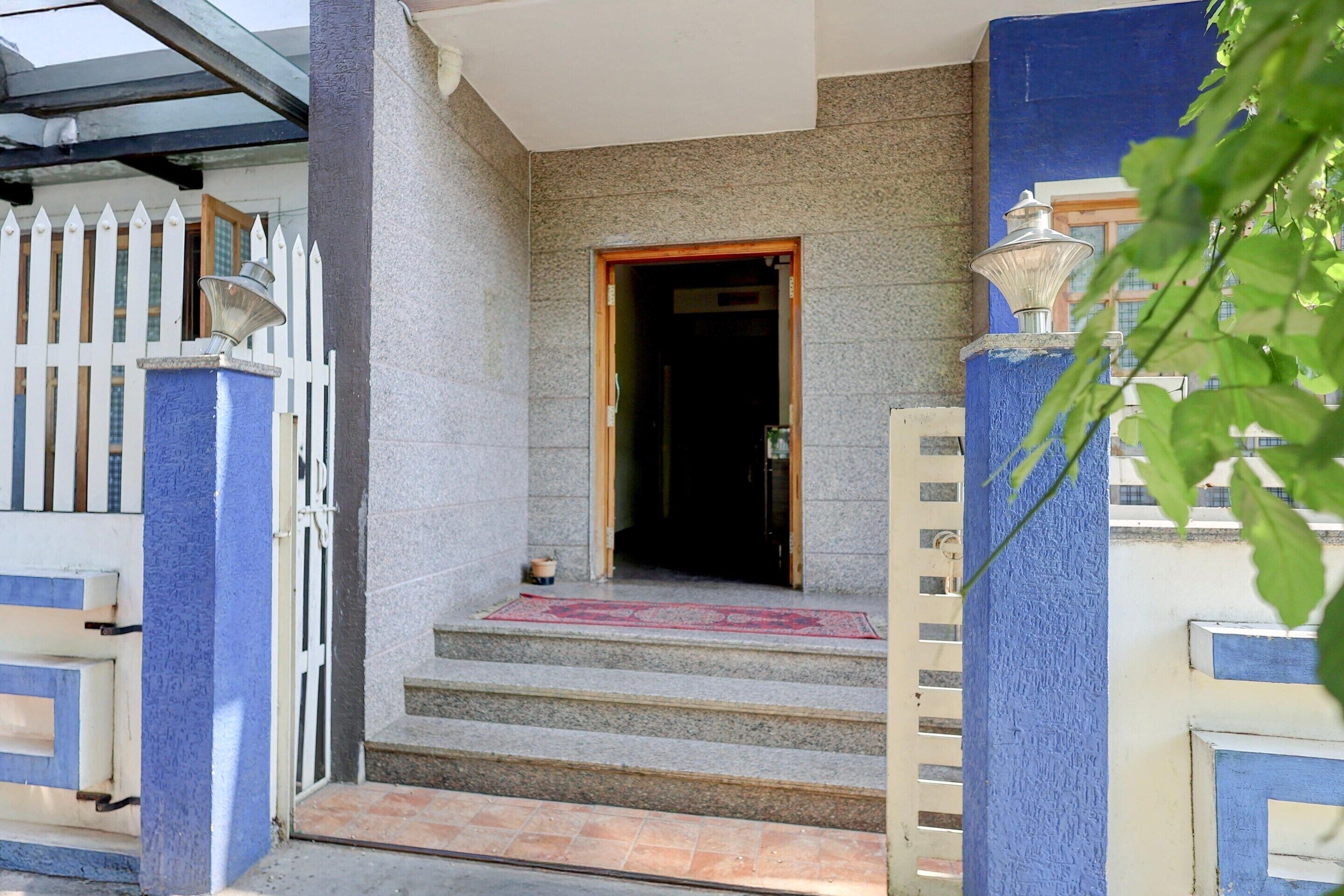 A building entrance with a white picket fence, a blue door, and steps leading up to a tiled area.
