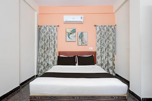 A hotel room with a bed, an air conditioner, two wall art pieces, and patterned curtains. - Collection O Mysore Gokulam (Mysore)