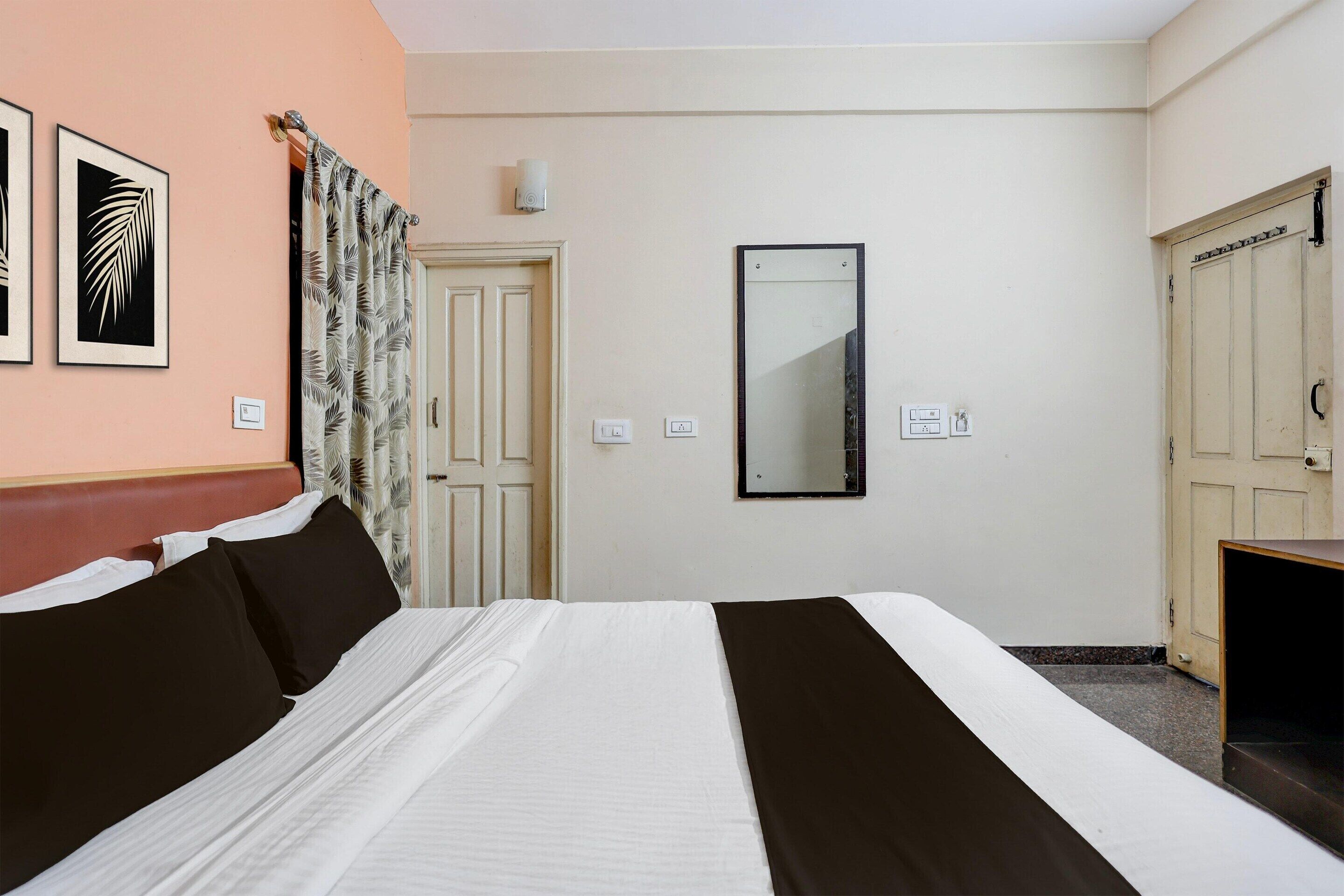 A hotel room with a bed, a door, a mirror, and a wall-mounted light fixture.