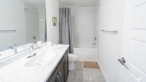 Une salle de bain avec deux lavabos, des toilettes, une baignoire et un rideau de douche.