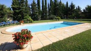 A swimming pool with a tiled deck, surrounded by a well-maintained lawn and tall trees. - Bastide Carpe Diem (Fabrègues)