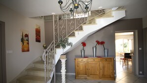 A staircase with a white balustrade and a chandelier, leading to a dining area with wooden cabinets and red flowers. - Bastide Carpe Diem (Fabrègues)