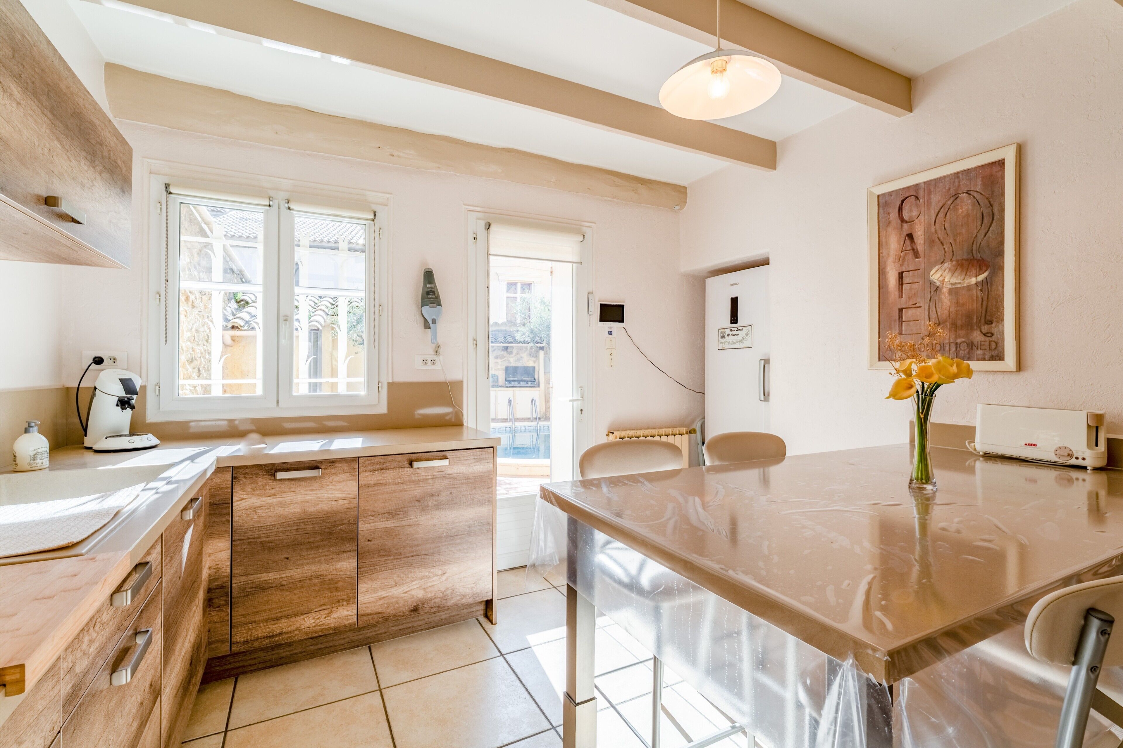 A modern kitchen with wooden cabinets, a marble countertop, and a view through large windows.