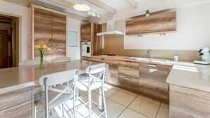 Een moderne keuken met houten kastjes, een centraal eiland met barkrukken, een inbouwoven en een hangende lamp.
