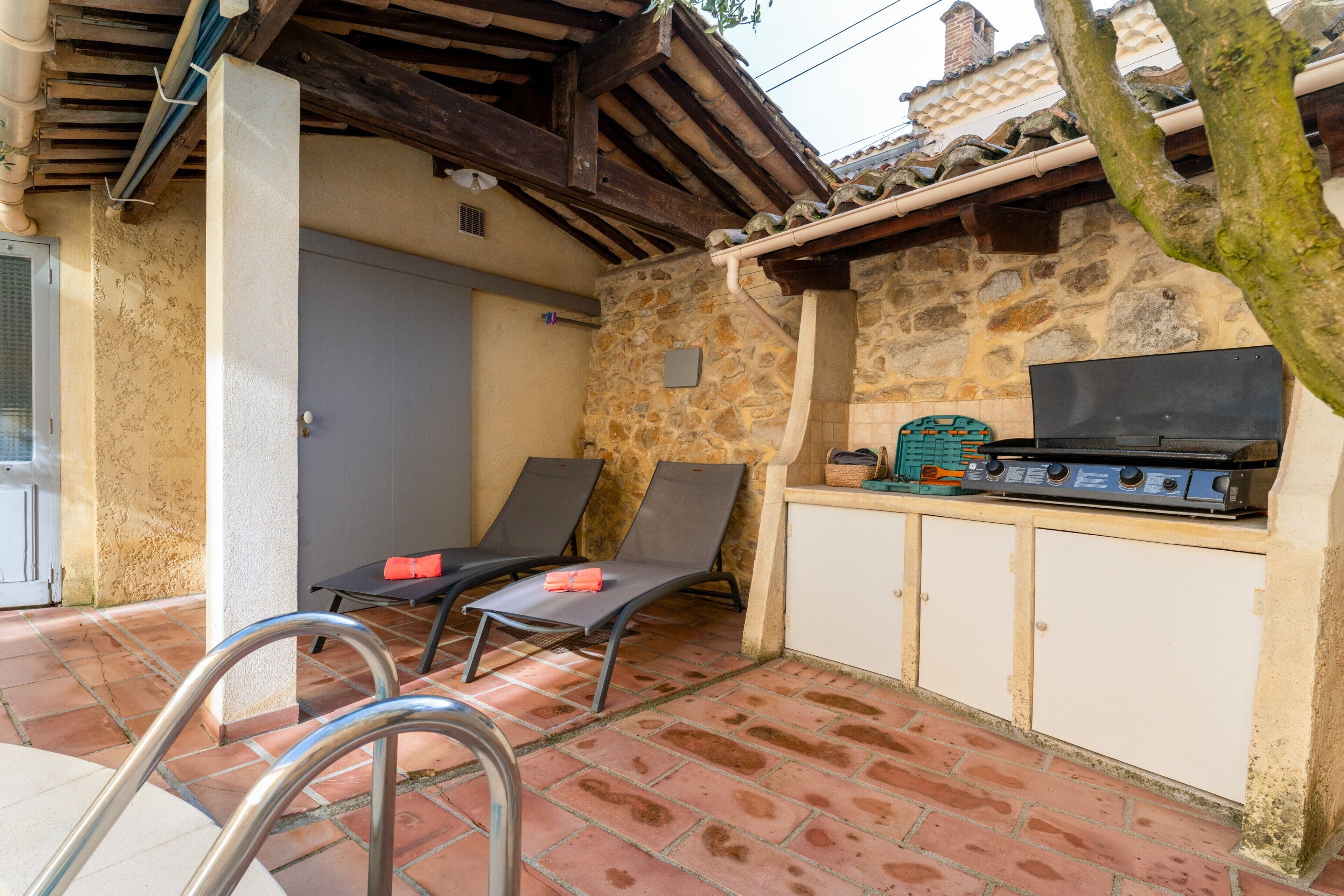 Een terras met een stenen muur, een barbecue en twee comfortabele stoelen.