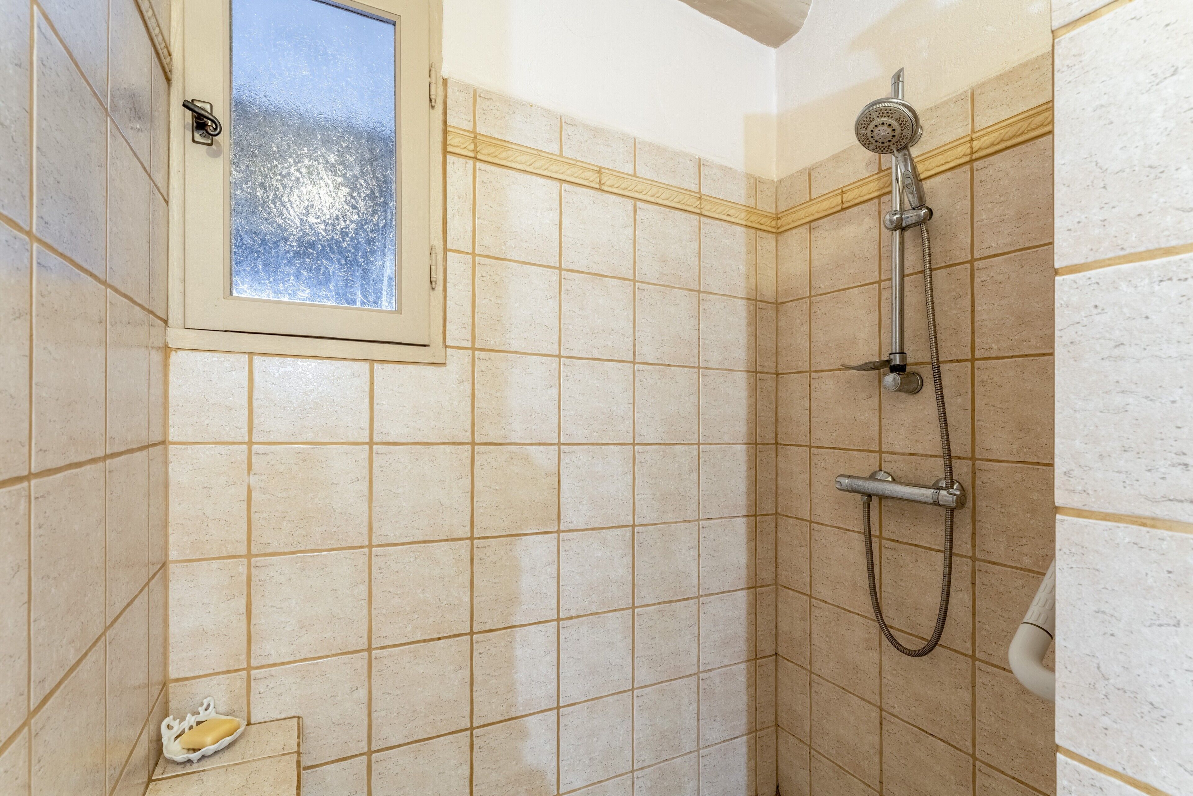 A shower with a handheld showerhead, a window, and a small soap dish.