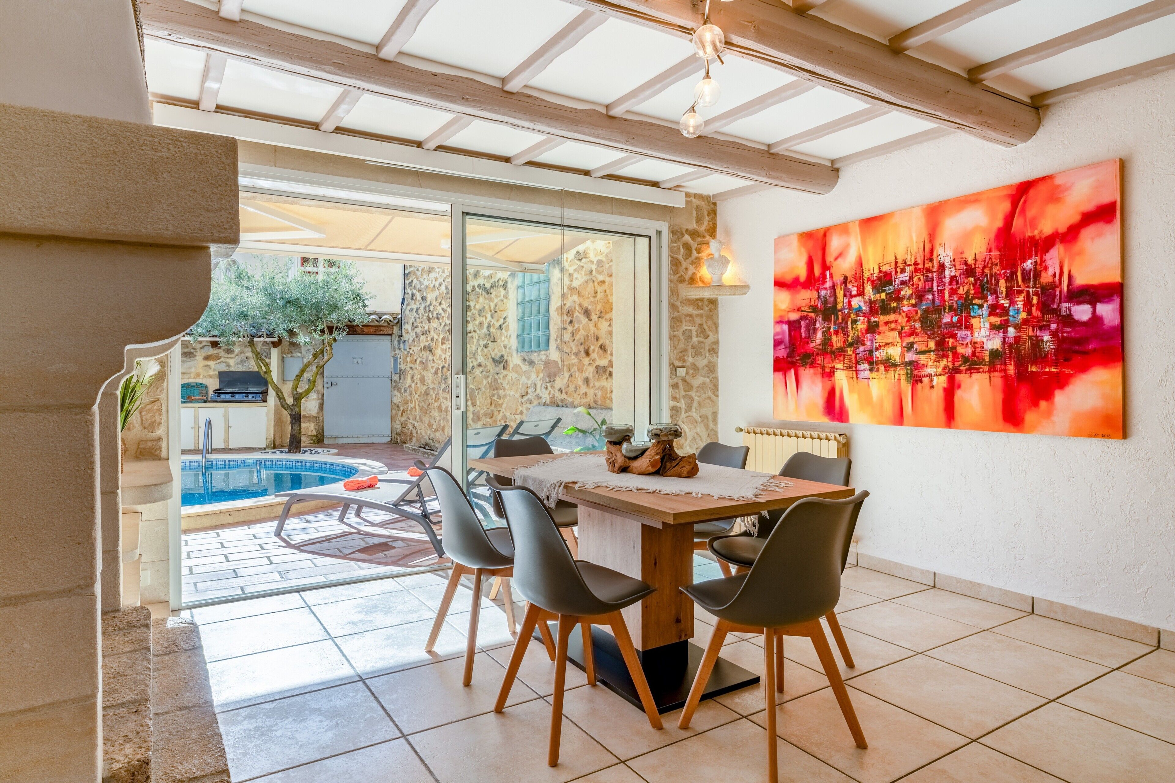 Un espace repas avec vue sur la piscine, des murs en pierre et un grand tableau abstrait.