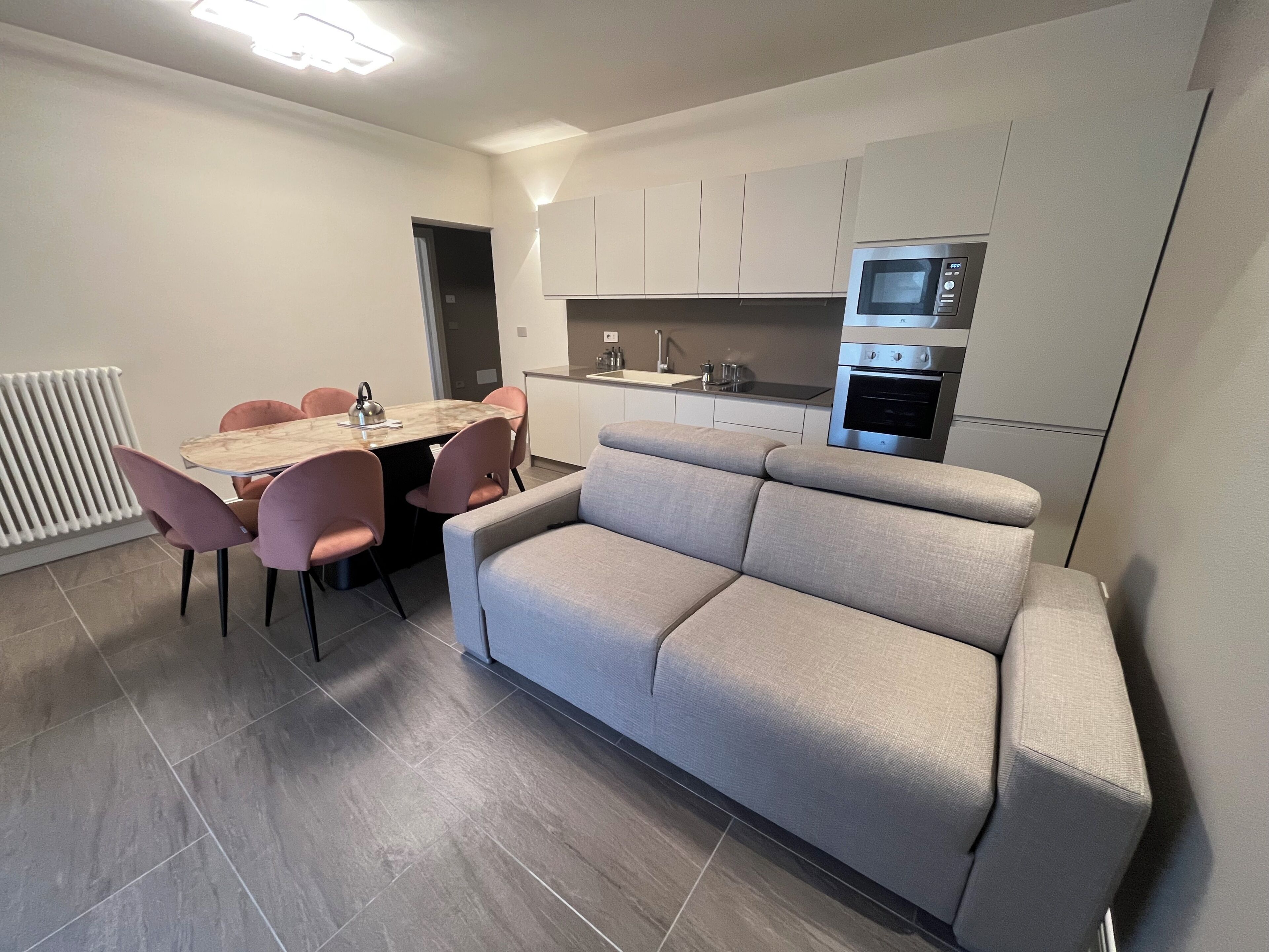 Um espaço compacto com mesa de jantar, cadeiras, sofá, cozinha compacta equipada com micro-ondas e forno, e um radiador.