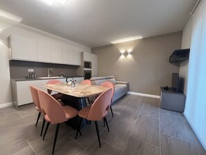Una cocina moderna con armarios blancos, una mesa de comedor con sillas rosadas y un sofá gris.