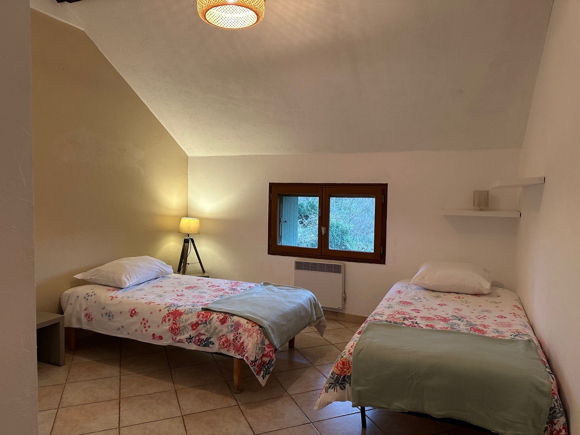A small, cozy bedroom with two single beds, a window, a radiator, and a lamp.