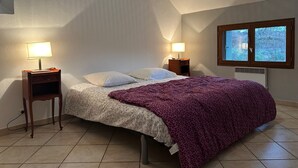 A bedroom with a bed, two bedside tables with lamps, a window, and a radiator.