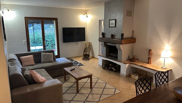 A living room with a sofa, a coffee table, a TV, a fireplace, and a dining area with chairs.