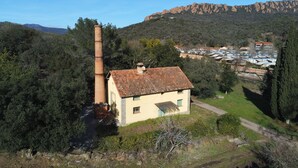 A rural house with a chimney, surrounded by trees and a mountain in the background.