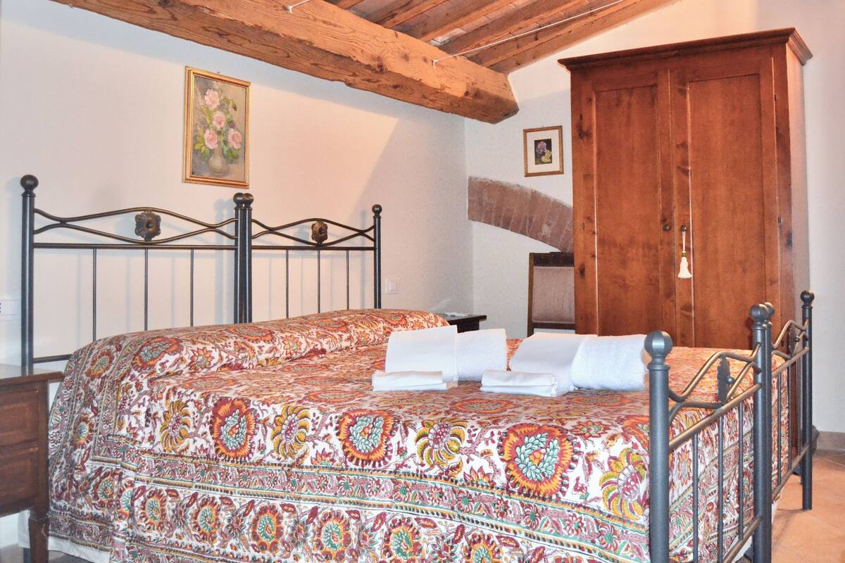 Un dormitorio con cama, vigas de madera en el techo, un armario de madera y un cuadro floral enmarcado en la pared.