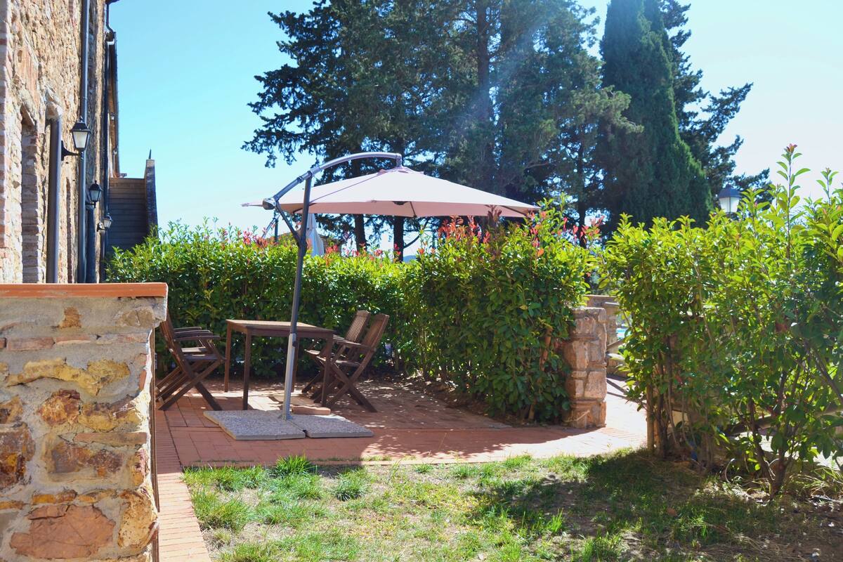 Un patio al aire libre con pared de piedra, muebles de madera y una pérgola con toldo.