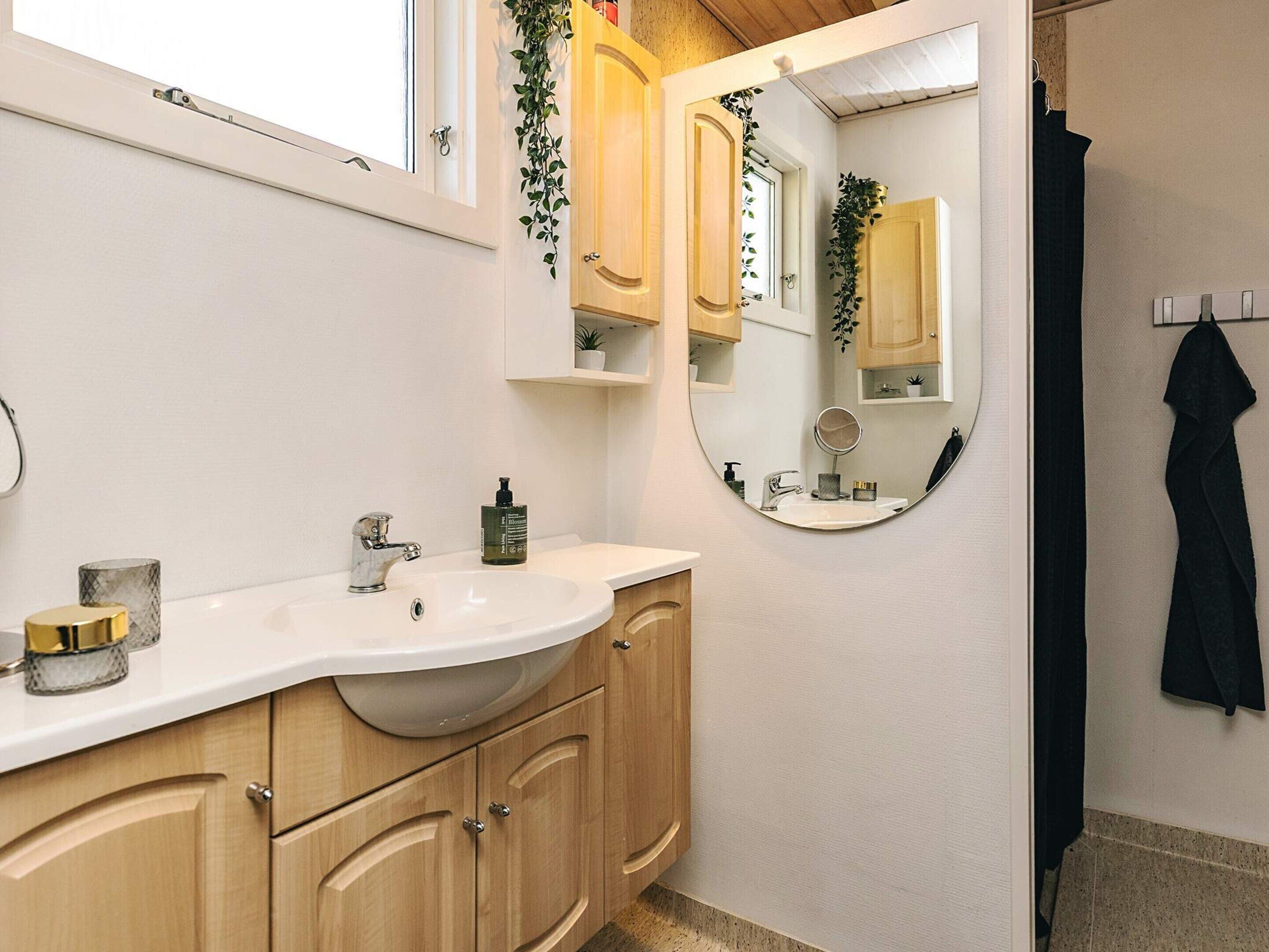 Ein Badezimmer mit weißem Waschbecken, Holzschränken, einem Spiegel und einem Handtuchhalter.