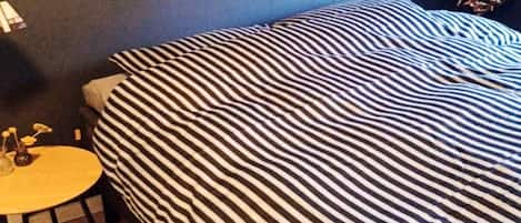 Una habitación con una cama con ropa de cama a rayas, una mesita redonda con un florero y una lámpara en una mesita de noche.