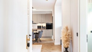 A modern kitchen with white cabinets, a black oven, and a dining area with grey chairs. - The Summit Suite I Meissen – Luxury Penthouse with Elbe and Cathedral Views (Meißen)