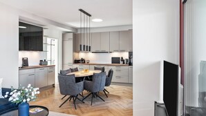 A modern kitchen with grey cabinets, a dining area with grey chairs, and a TV mounted on the wall. - The Summit Suite I Meissen – Luxury Penthouse with Elbe and Cathedral Views (Meißen)