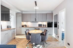 A modern kitchen with grey cabinets, a round dining table with grey chairs, and a pendant light. - The Summit Suite I Meissen – Luxury Penthouse with Elbe and Cathedral Views (Meißen)