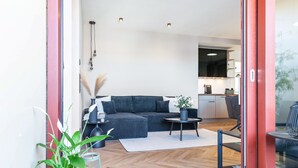 A modern living room with a sofa, a small round table, and a potted plant. - The Summit Suite I Meissen – Luxury Penthouse with Elbe and Cathedral Views (Meißen)
