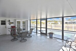 Ein Zimmer mit Esstisch und Stühlen, einem Grill und großen Fenstern mit Blick auf einen Pool und einen Außenbereich.