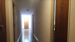 Ein schmaler, gut beleuchteter Korridor mit Holztüren auf beiden Seiten und einer Lichtquelle am Ende.