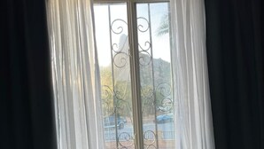 Una habitación con una cama, una ventana con barrotes y cortinas translúcidas.