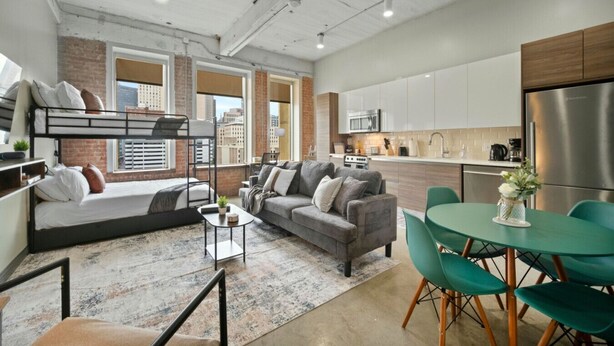 Un apartamento moderno con una cama alta, un sofá, zona de comedor y cocina.
