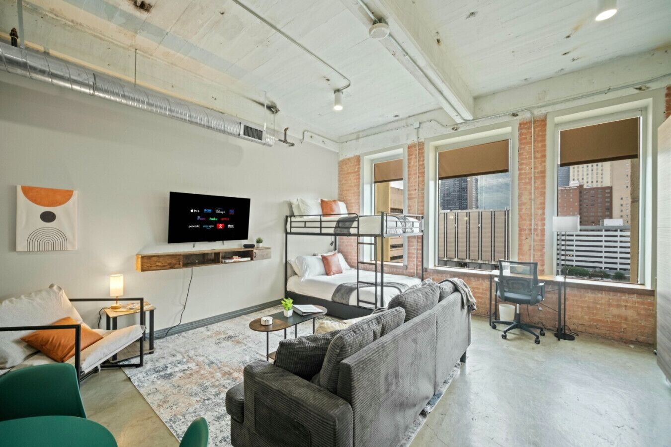 A modern hotel room with a bunk bed, a sofa, a TV, and a desk with a computer.