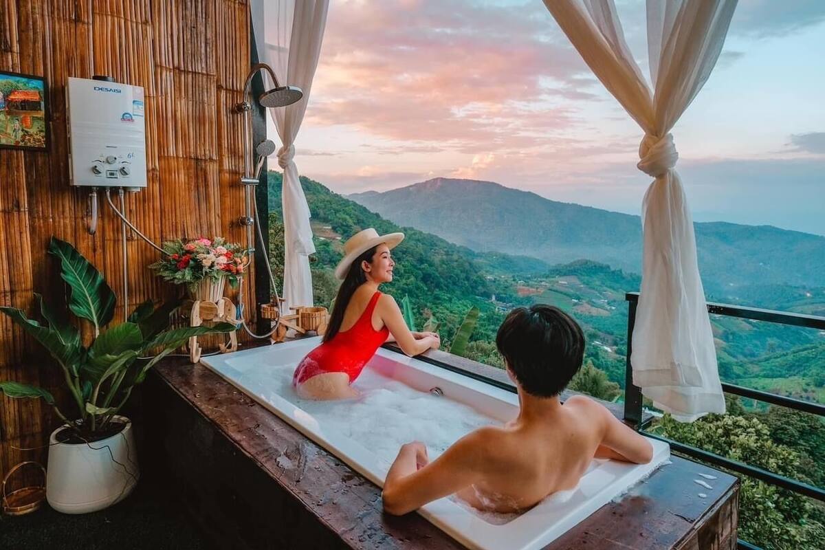 Un couple se détend dans un bain à remous avec vue sur les montagnes, entouré d’un mur en bambou et d’un chauffe-eau.