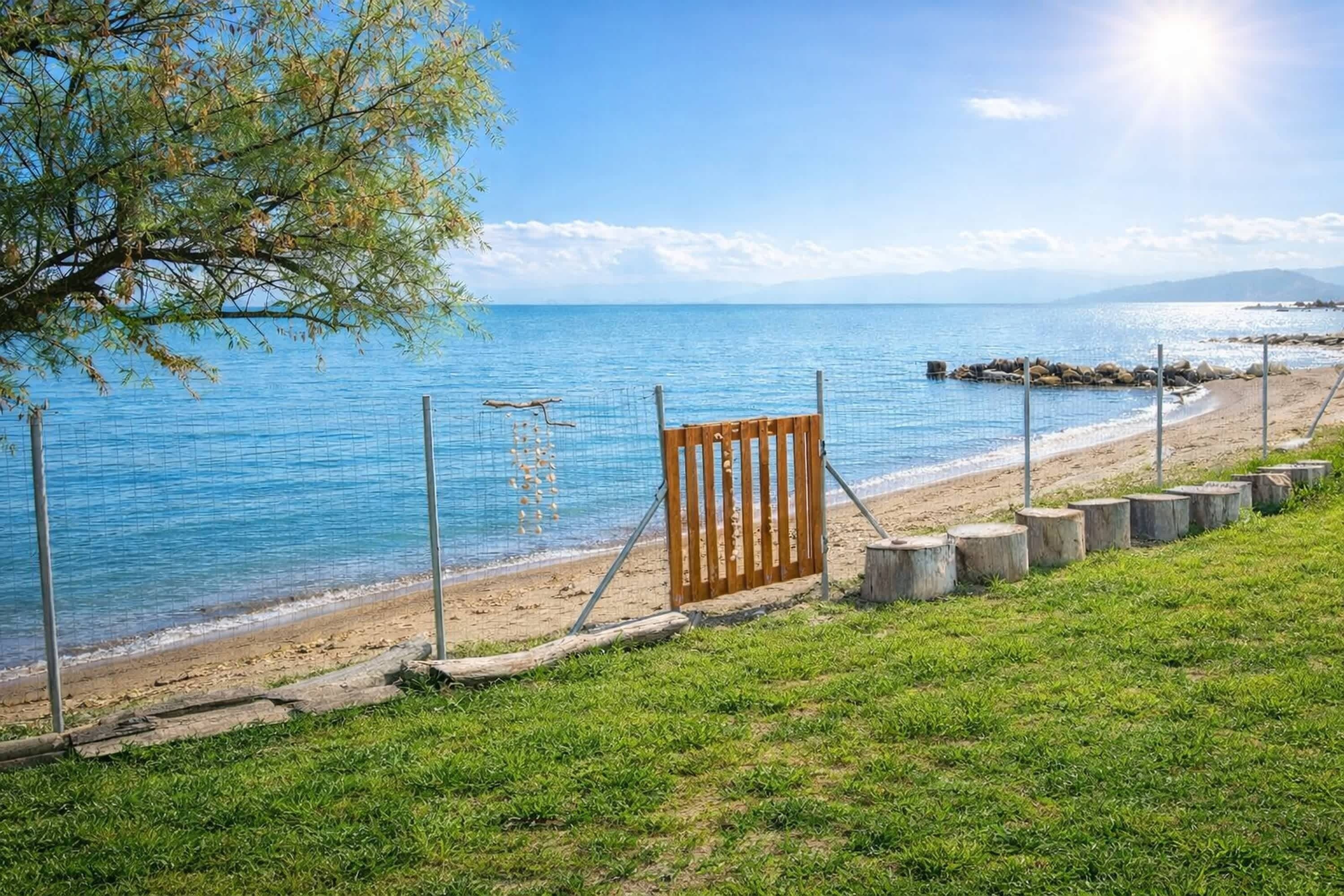 A beach with a wooden gate, a grassy area, and a clear blue sea.