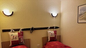 Hotelkamer met twee bedden, elk met een rode sprei en bijpassende kussens. Boven de bedden zitten wandlampen en er hangt een schilderij aan de muur.