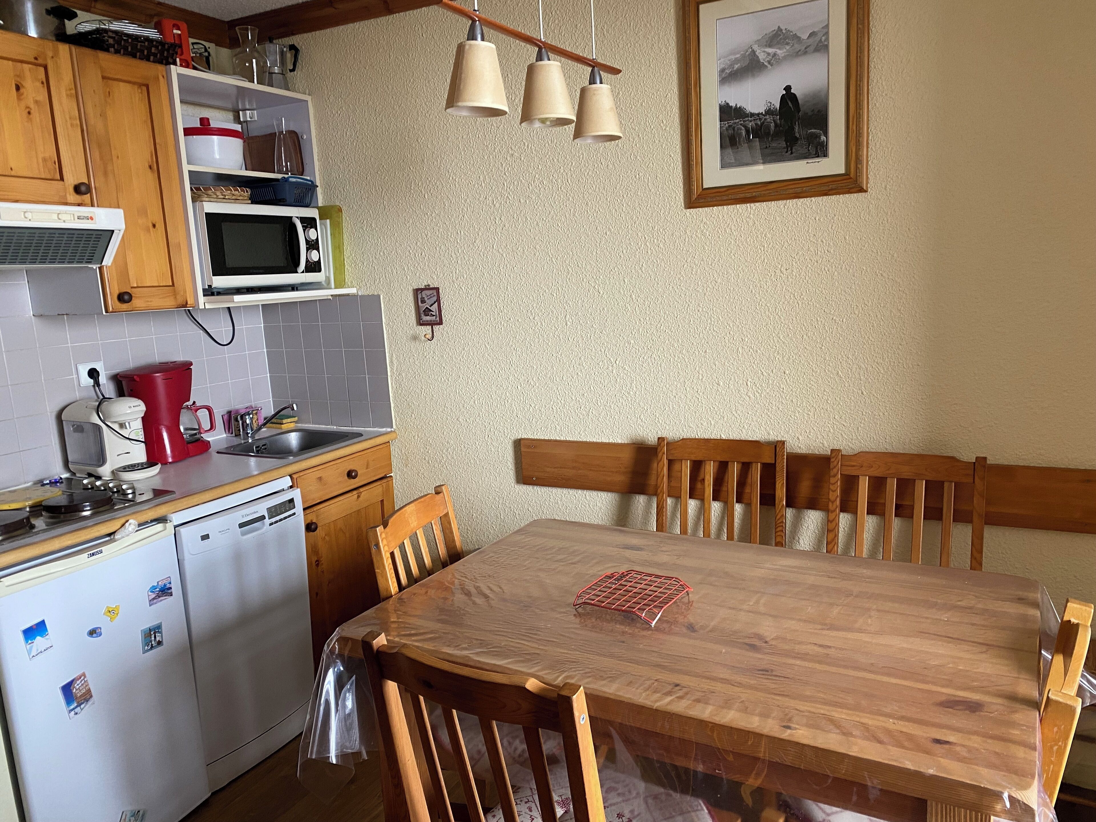 A kitchen with wooden cabinets, a microwave, a coffee maker, and a dining table with chairs.