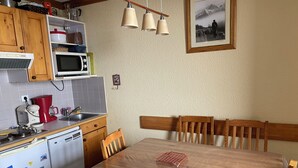 Een keuken met houten kastjes, een magnetron, een koffiezetapparaat en een eettafel met stoelen.