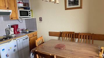 A kitchen with wooden cabinets, a microwave, a coffee maker, and a dining table with chairs.