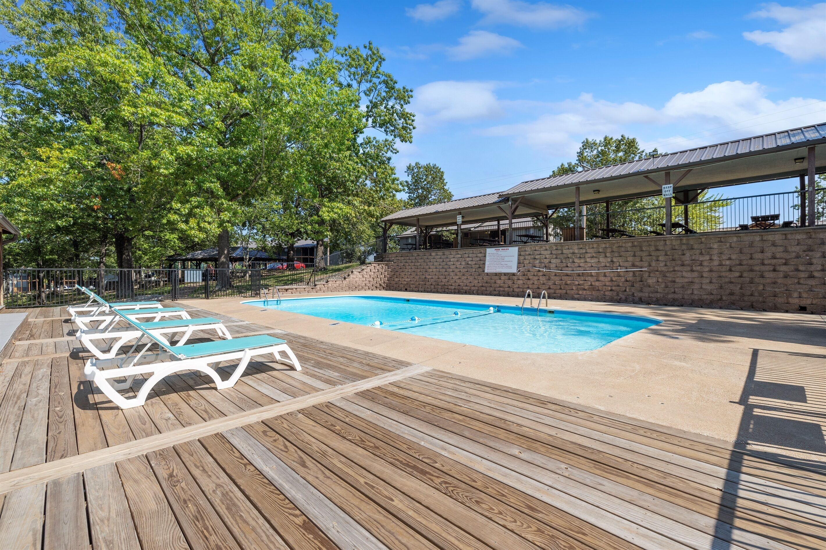 Una terraza de madera con piscina, sillones de descanso y un área de estar cubierta.