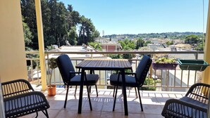 A balcony with a wooden table and four chairs, overlooking a residential area with trees and buildings. - Zenozy Luxury Apartments - Corfu Town (Kerkira)