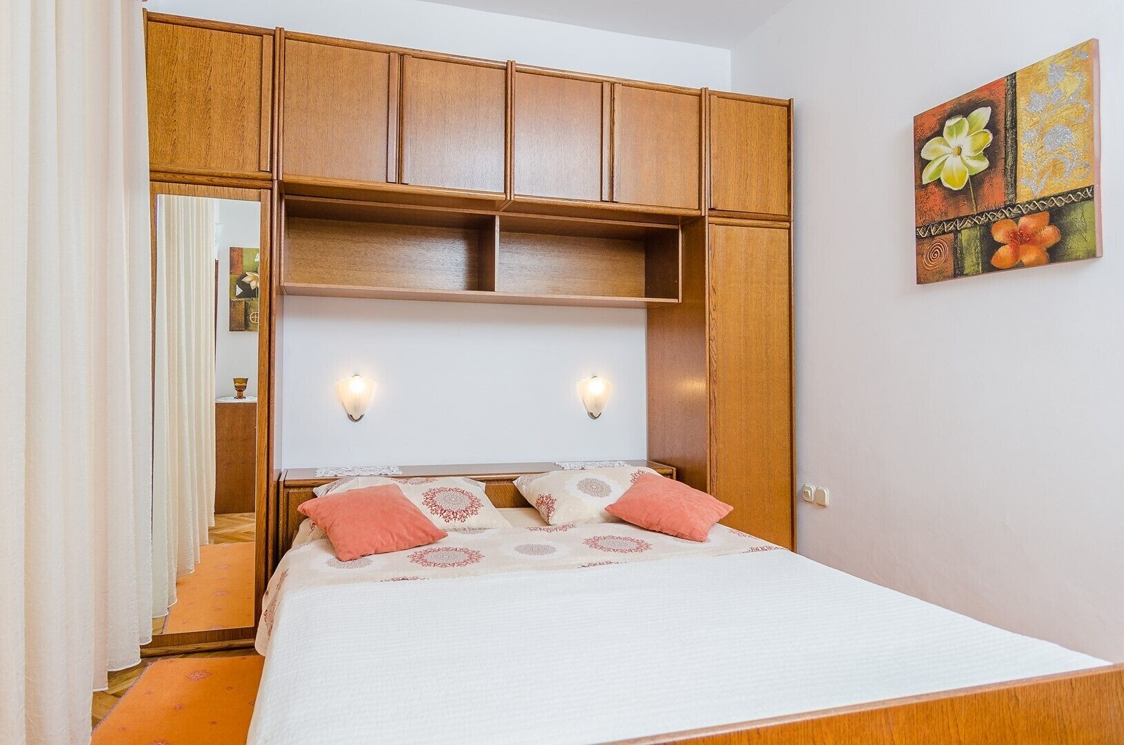 Une chambre à coucher avec un lit, une tête de lit en bois, deux appliques murales et un tableau.