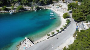 Luftaufnahme einer Küstenlandschaft mit Booten, die an der Uferlinie liegen, einer asphaltierten Straße und freiem Blick auf den Strand.