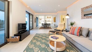 Un salon moderne avec un canapé, un fauteuil, une table basse et, au fond, un coin repas.