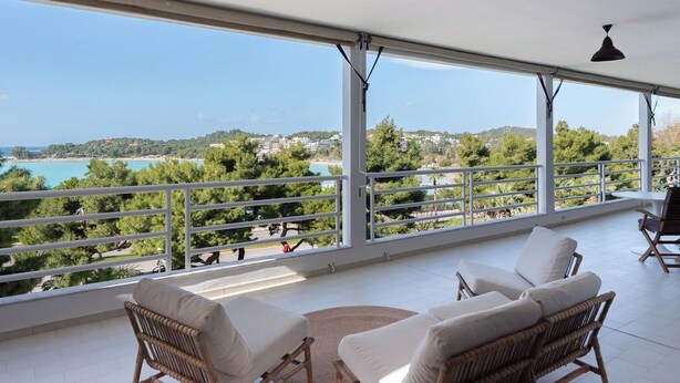 Un balcon agrémenté de meubles en osier, une vue sur la mer et un ciel dégagé.