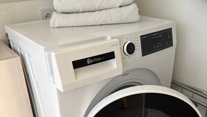 A front-loading washing machine with a control panel, stacked towels, and a wooden cabinet. - Modernes Apartment für Urlaub oder Monteuraufenthalt (Bebra)