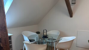A modern dining area with a glass table surrounded by white chairs, a small plant, and a hanging light fixture. - Modernes Apartment für Urlaub oder Monteuraufenthalt (Bebra)