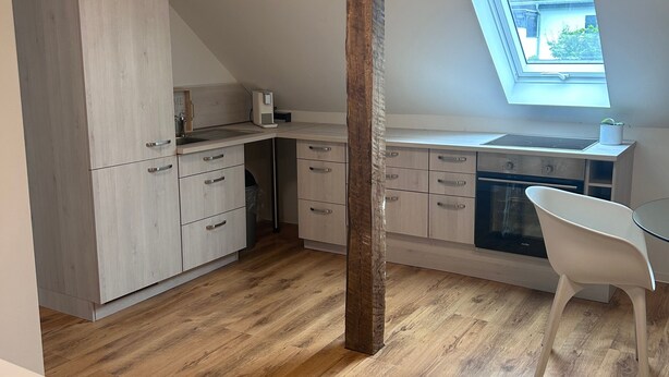 A modern kitchen with wooden flooring, a skylight, and a white dining area. - Modernes Apartment für Urlaub oder Monteuraufenthalt (Bebra)