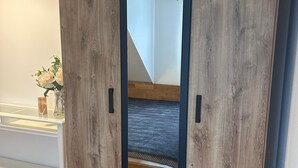 A room with a wooden wardrobe, a bed with a patterned bedspread, and a bedside table with a vase of flowers. - Modernes Apartment für Urlaub oder Monteuraufenthalt (Bebra)