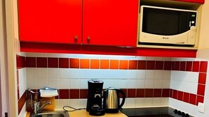 Ett kompakt kök med röda skåp, en mikrovågsugn, en kaffebryggare och en diskmaskin.