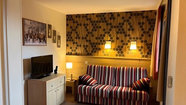 Ett mysigt rum med en randig soffa, en tv-apparat på ett skåp och en vägg med hexagonala mönster.